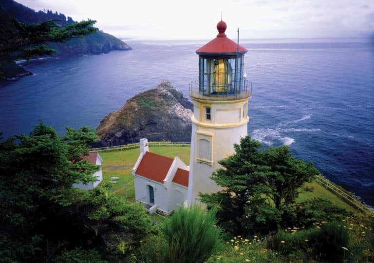 An aerial shot of Haceta Head Lighthouse on the Oregon coast with with Pacific Ocean in the background.